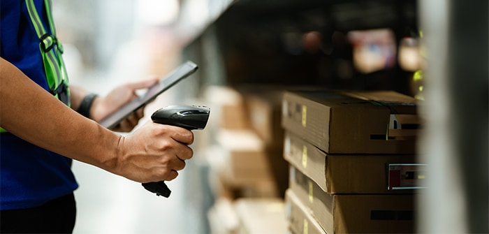 A worker in a warehouse scanning a barcode to send data to a tablet